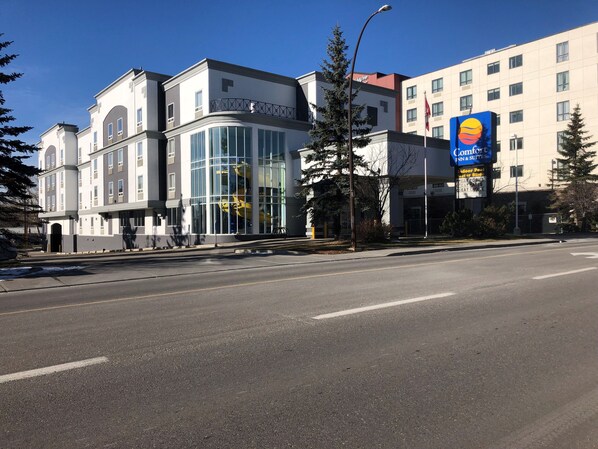 A modern hotel with a large glass facade, a prominent Comfort Inn & Suites sign, and a clear blue sky.