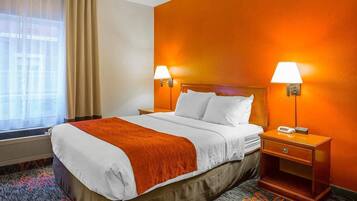 Una habitación de hotel con una cama, dos mesitas de noche, un ventanal con cortinas y una lámpara de pared.
