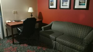 Habitación de hotel con escritorio, silla y sofá. Hay tres cuadros en la pared.