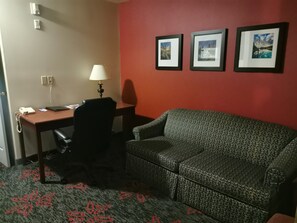 A hotel room with a desk, chair, and a sofa. There are three framed pictures on the wall.