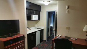 Habitación de hotel compacta con kitchenette, televisor de pantalla plana, escritorio con teléfono y una silla.