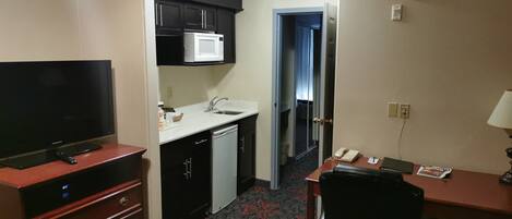 Une chambre d’hôtel compacte comprenant un coin cuisine, un téléviseur à écran plat, un bureau avec un téléphone et une chaise.