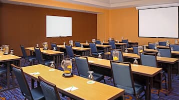 Un salón de conferencias con varias mesas, sillas y una pantalla para proyector.
