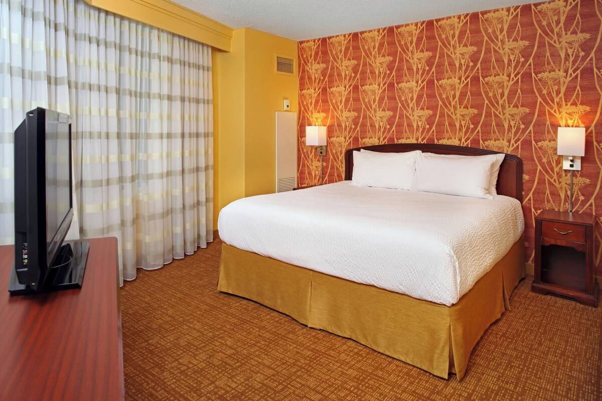 Habitación de hotel con una cama grande, un televisor sobre un escritorio de madera y dos lámparas de noche.