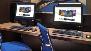Un espacio de trabajo en un hotel con dos monitores, un teclado, un ratón y una silla azul.