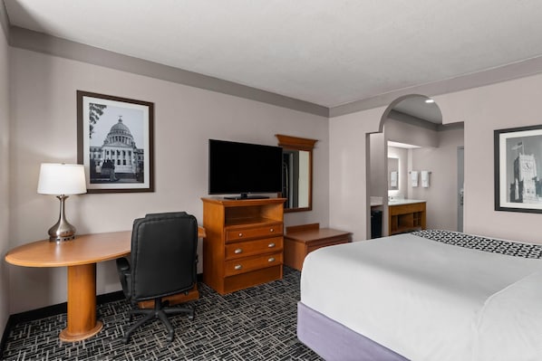 A hotel room with a bed, a desk with a chair, a television, a dresser, and framed pictures on the walls. - La Quinta Inn & Suites by Wyndham Jackson Airport/Pearl (Pearl)