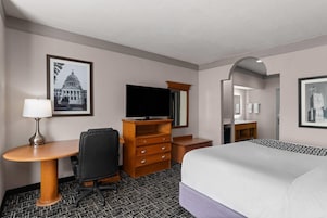 Habitación de hotel con cama, escritorio con silla, televisor, cómoda y cuadros en las paredes.