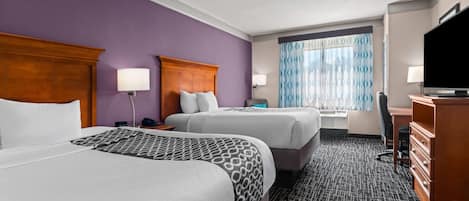 A hotel room with two beds, a television, a desk, and a window with curtains.