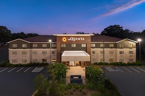 Un hotel con techo plano, entrada cubierta y estacionamiento con espacios delimitados.
