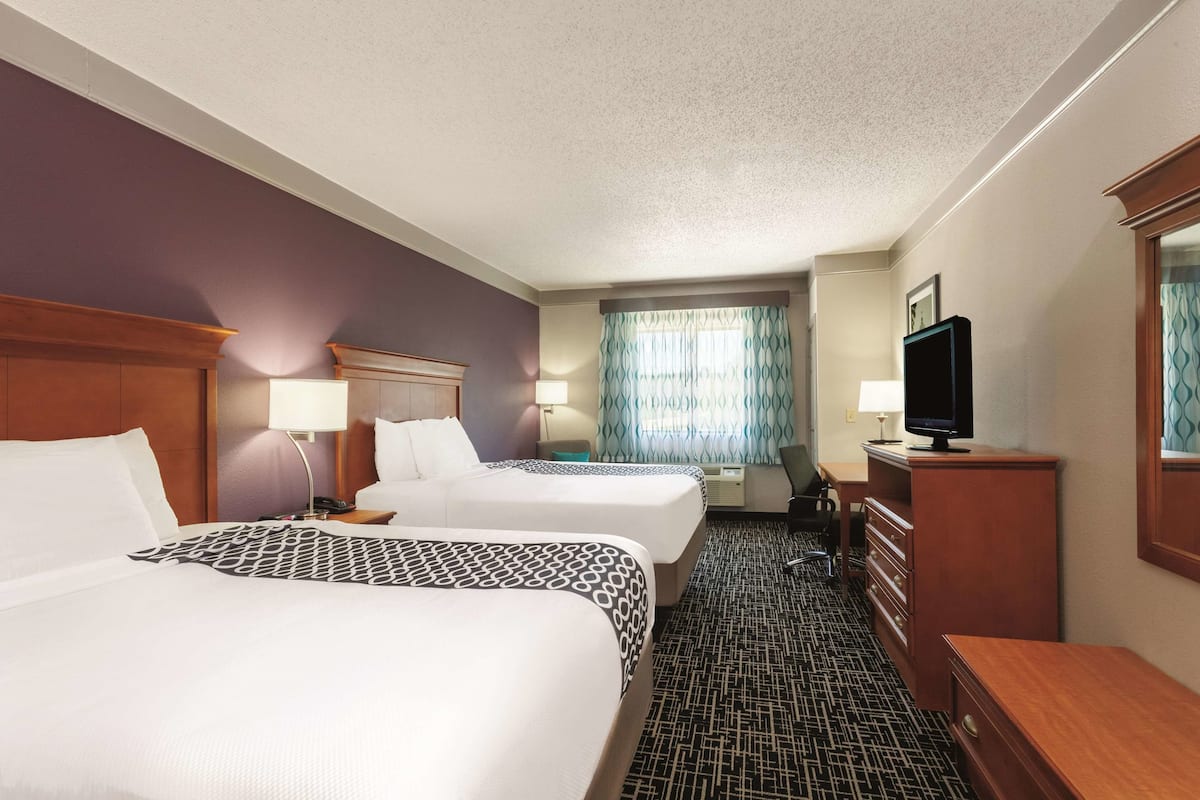 Une chambre d’hôtel avec deux lits, un bureau, une télévision et une commode.