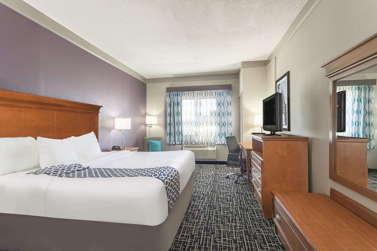 Une chambre d’hôtel avec un grand lit, un bureau, une chaise, une télévision et une commode.