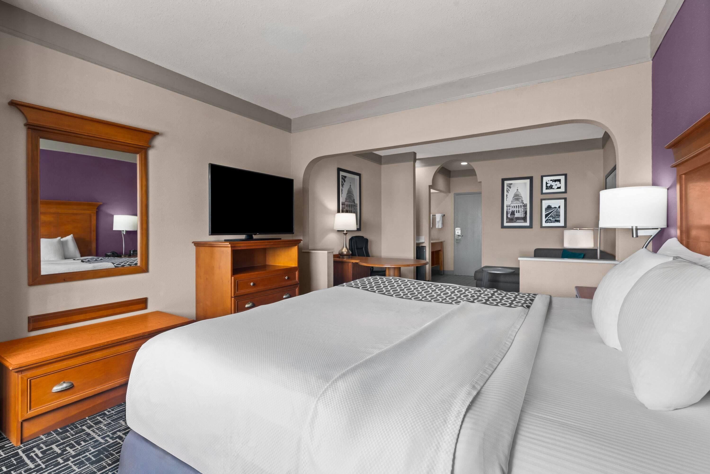 A hotel room with a large bed, a television, a desk, and a bathroom visible through an archway.
