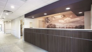 A reception area with a wooden reception desk, a mural of a landscape, and a tiled floor. - La Quinta Inn & Suites by Wyndham Jackson Airport/Pearl (Pearl)