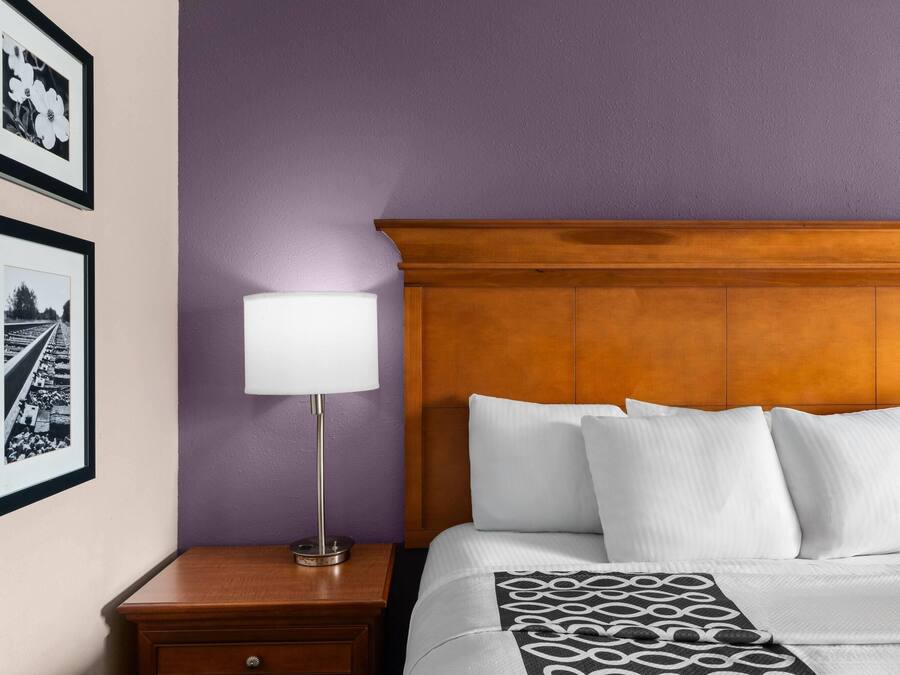 A hotel room with a wooden headboard, a nightstand with a lamp, and two framed pictures on the wall.