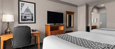Una habitación de hotel con una cama, un escritorio con lámpara, una televisión, un espejo y un cuadro en la pared.