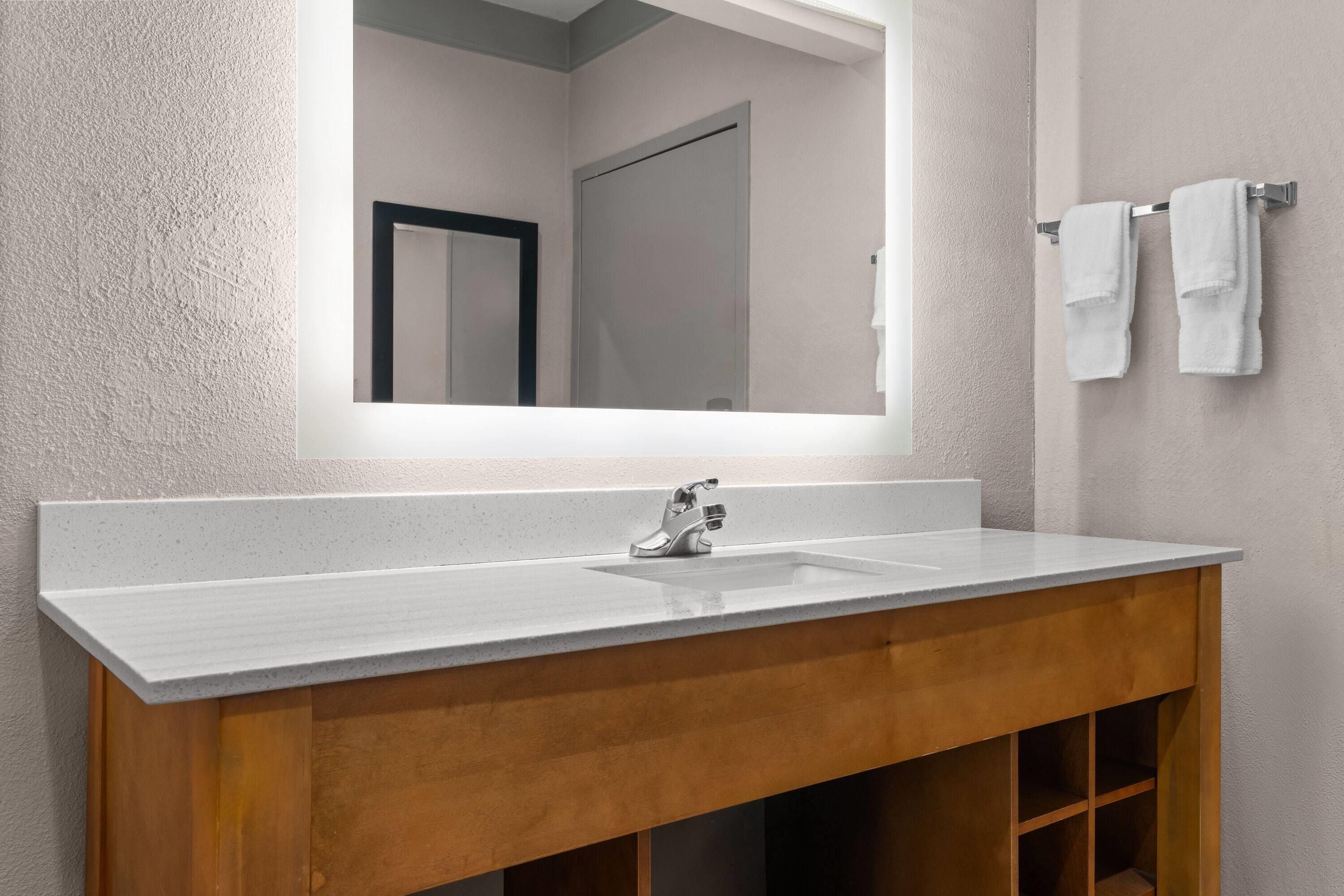 A bathroom with a white sink, wooden vanity, and a mirror.