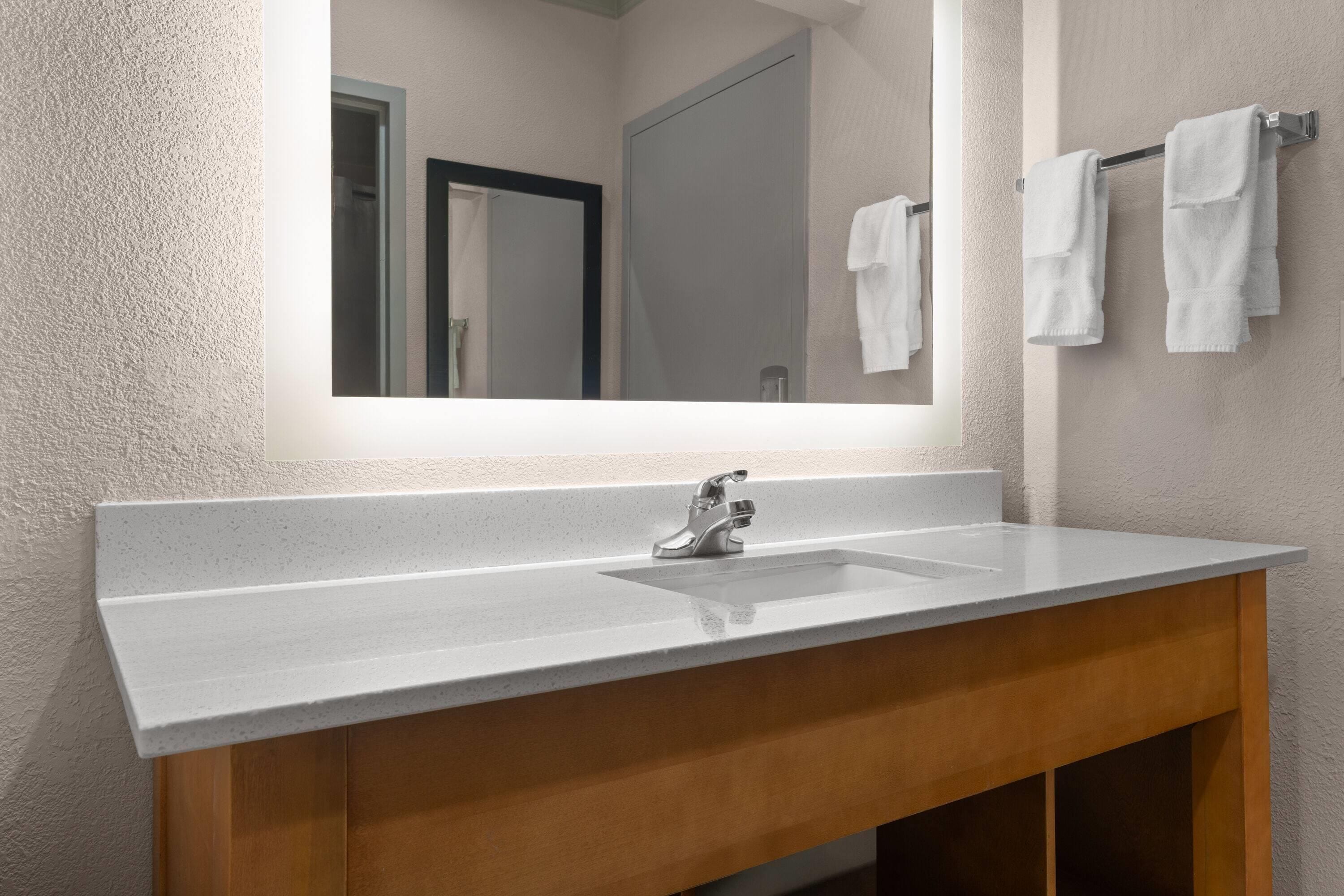 A bathroom with a large mirror, a sink, and two towels hanging on a rack.