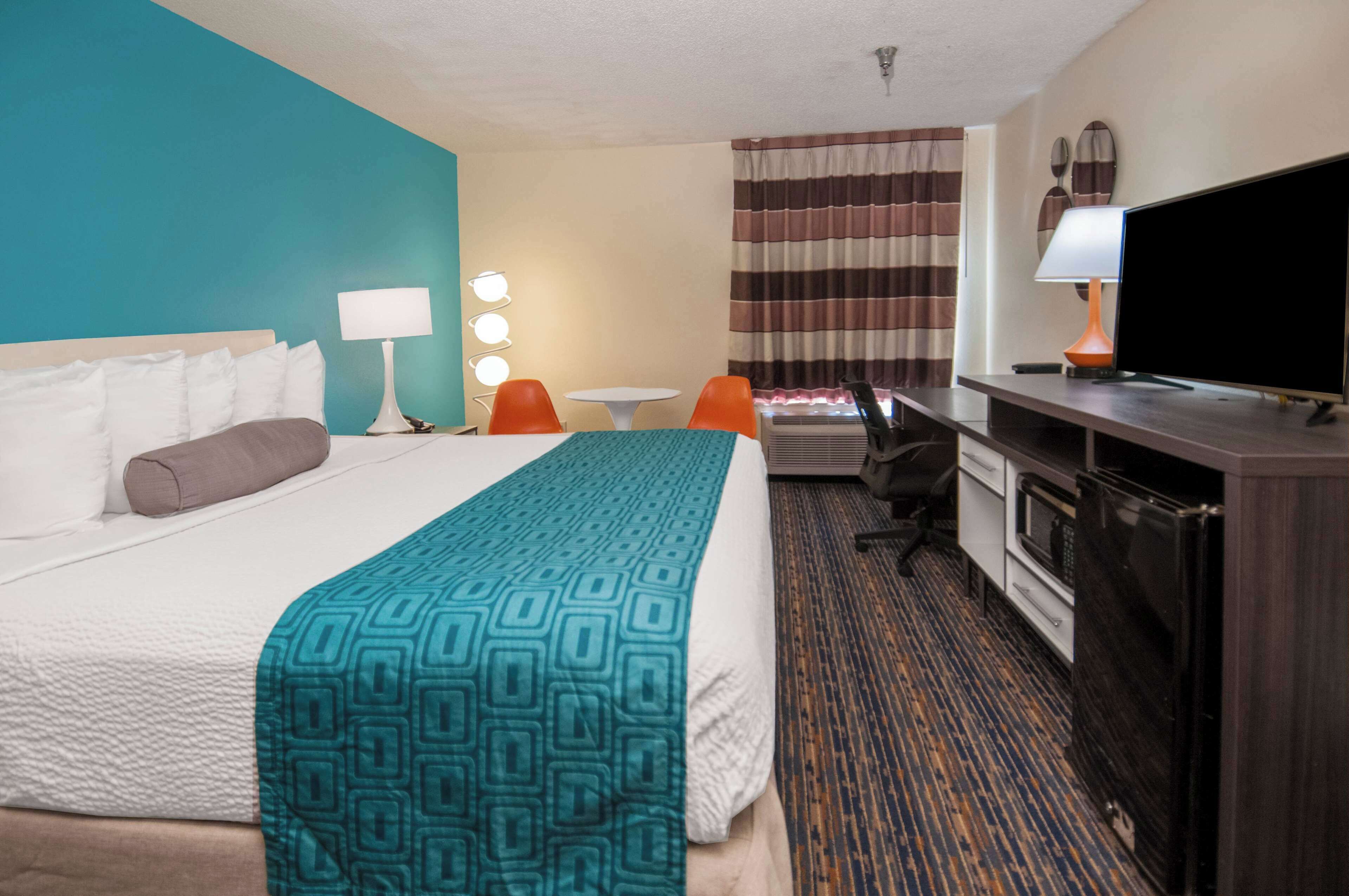 A hotel room with a bed, a desk with a computer, a television, and a small table with chairs.