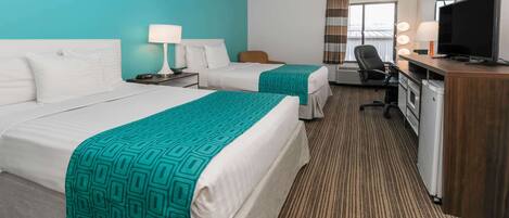 A hotel room with two beds, a desk with a TV, and a seating area with a lamp.