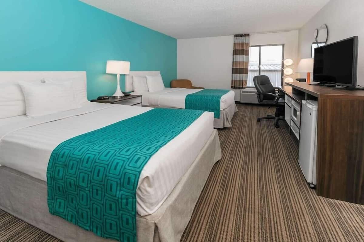 A hotel room with two beds, a desk with a TV, a chair, and a window with curtains.