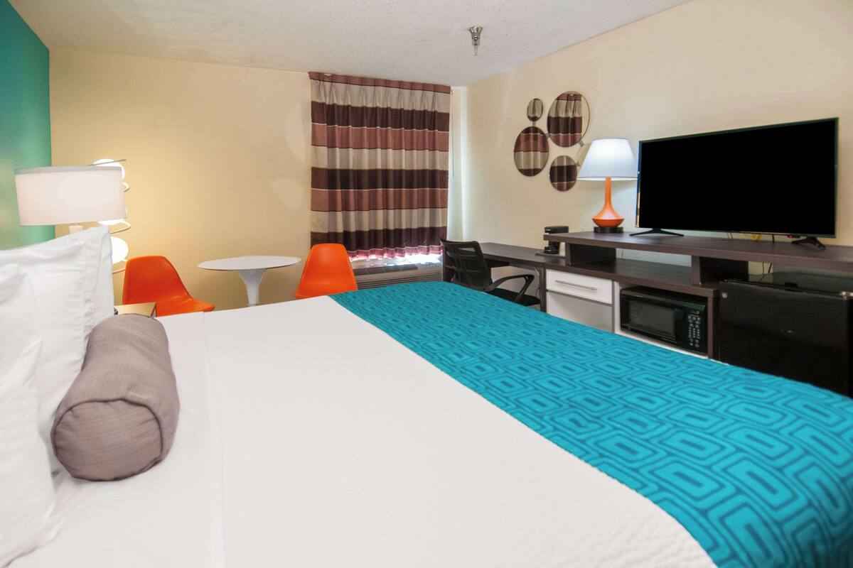 A hotel room with a bed, a desk, a chair, a TV, and a microwave.