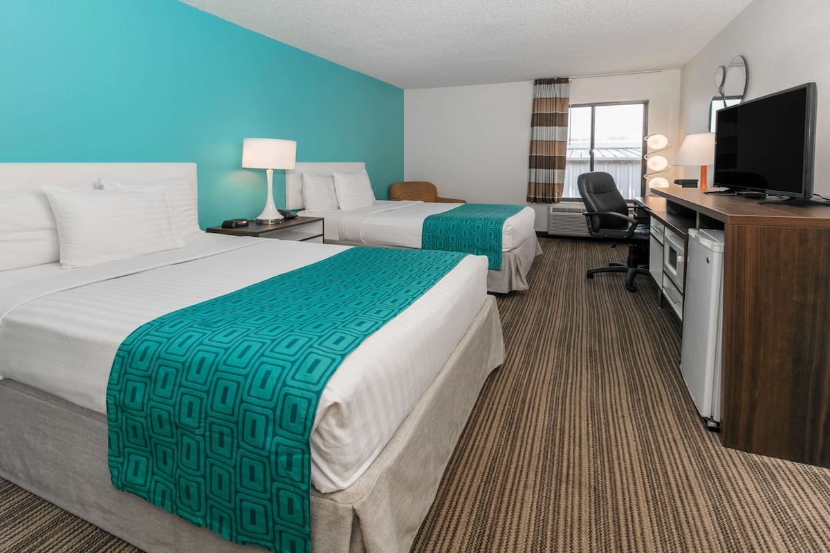 A hotel room with two beds, a desk, a TV, and a window with curtains.