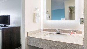 Une salle de bain avec un lavabo sur un meuble en granit, un miroir et un téléviseur posé sur un meuble en bois foncé.