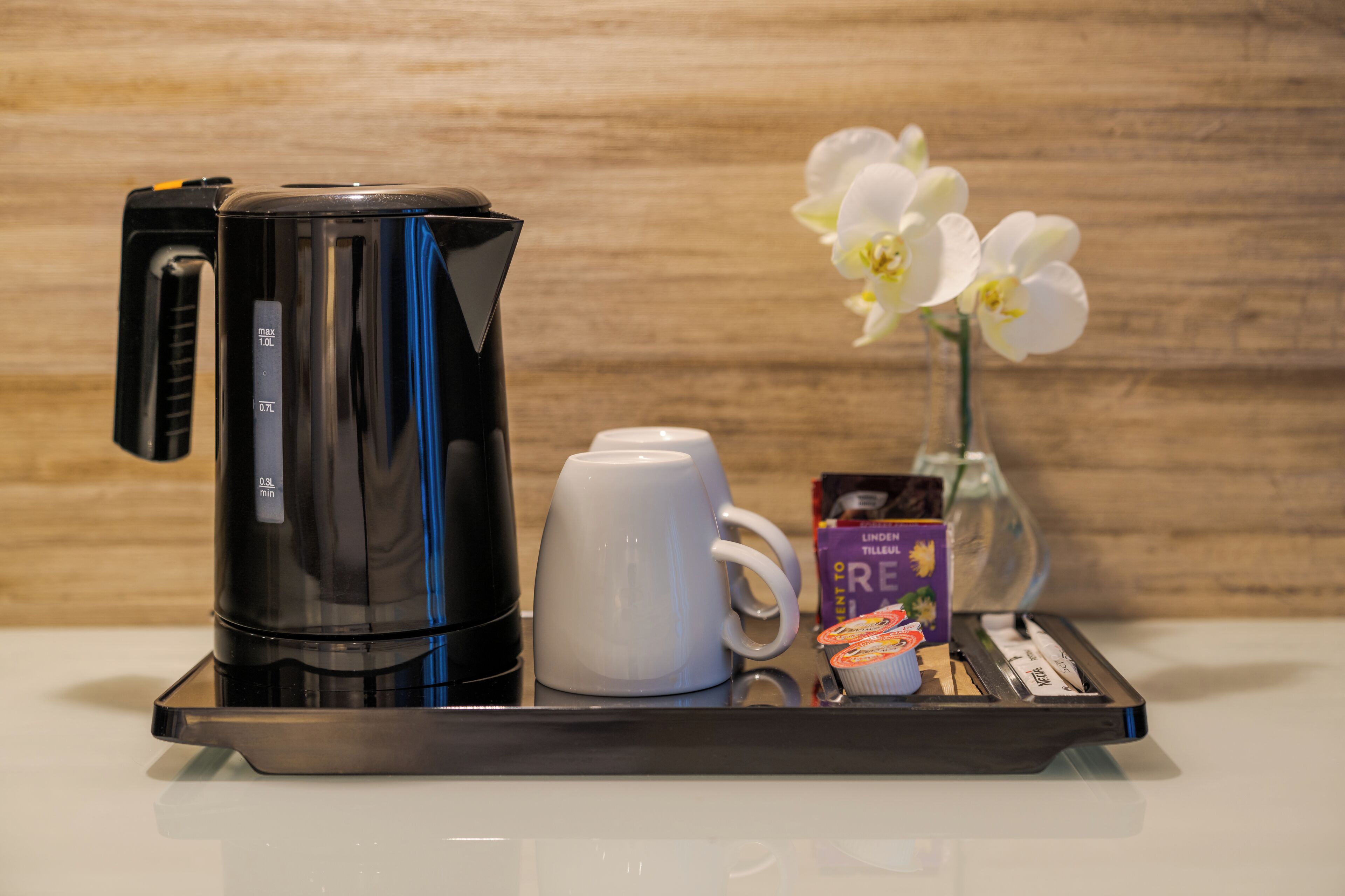 A coffee maker, a white mug, a glass vase with white flowers, and a box of Lindt chocolate on a tray.