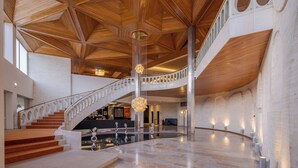 Un'ampia hall con soffitto in legno, una scalinata centrale e una reception.