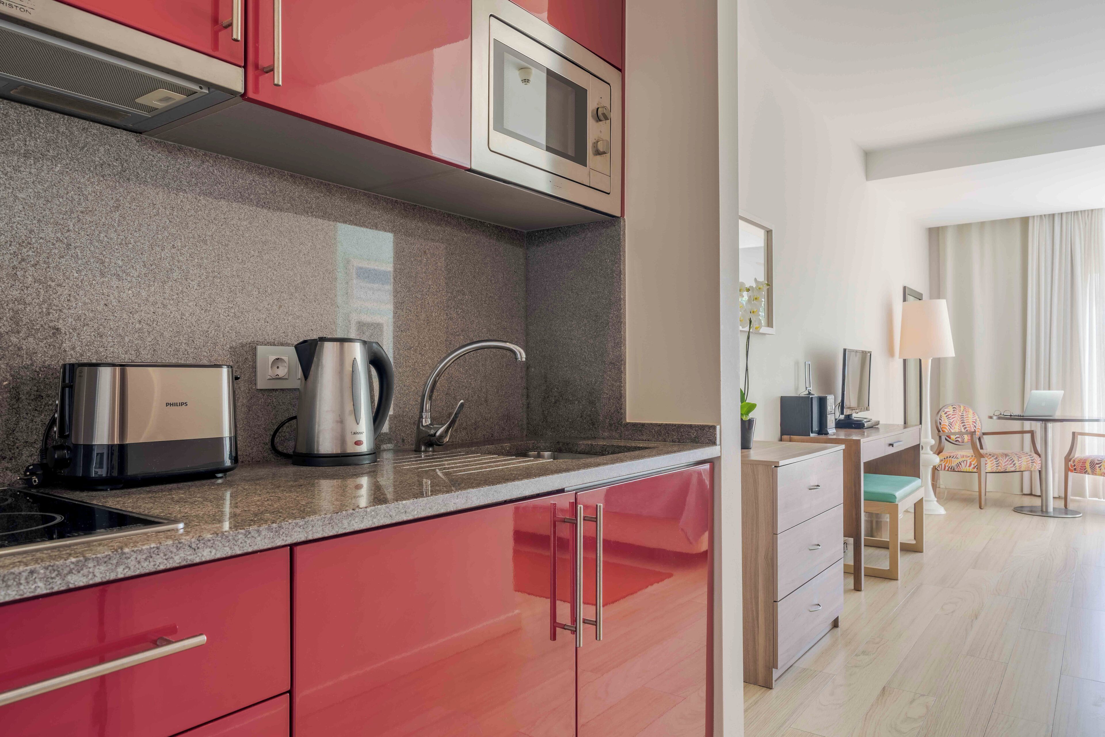 A modern kitchen with a microwave, coffee maker, and sink. There is a dining area with a table and chairs.