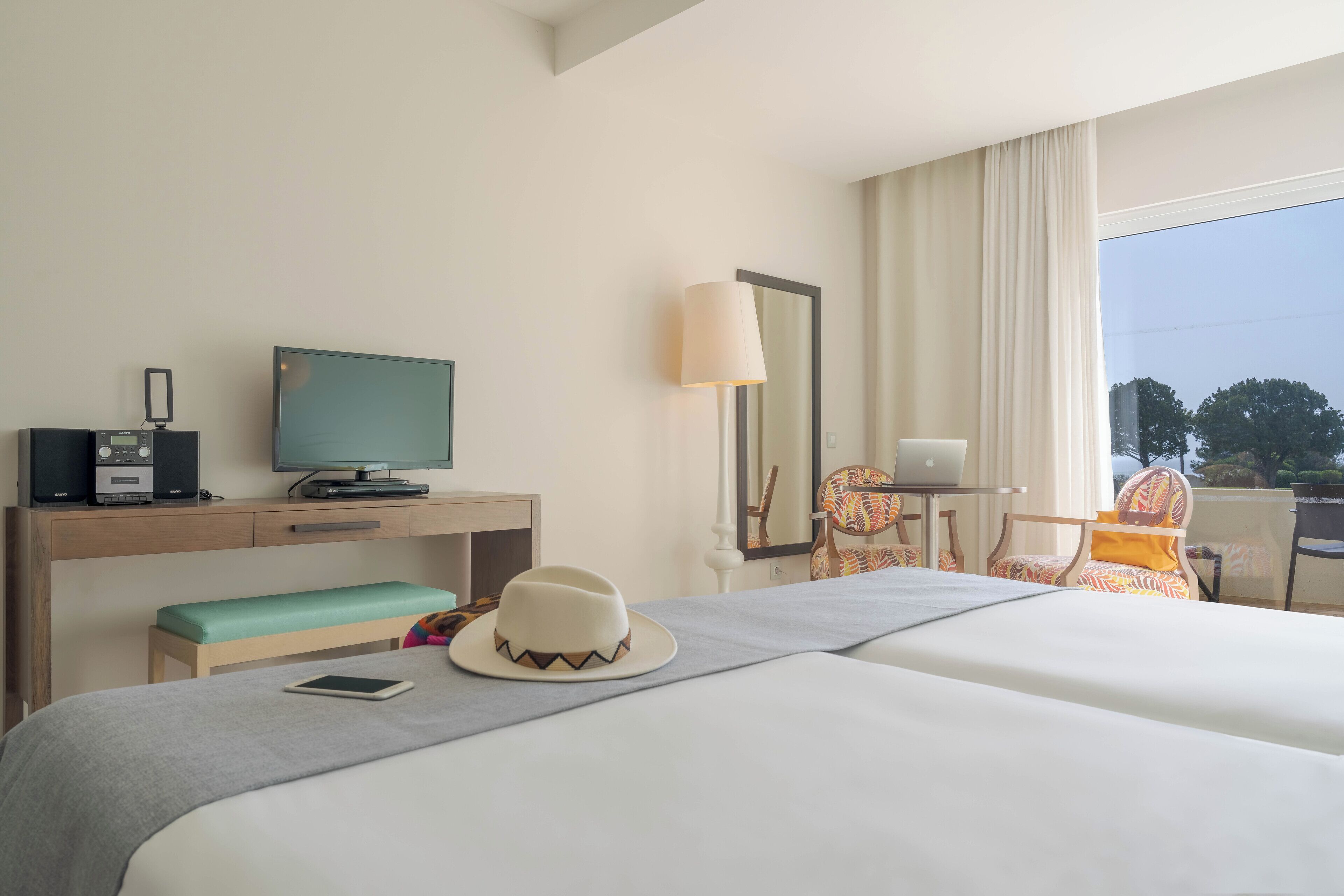Une chambre d’hôtel avec un lit, un bureau équipé d’une télévision, un ordinateur portable et une chaise.