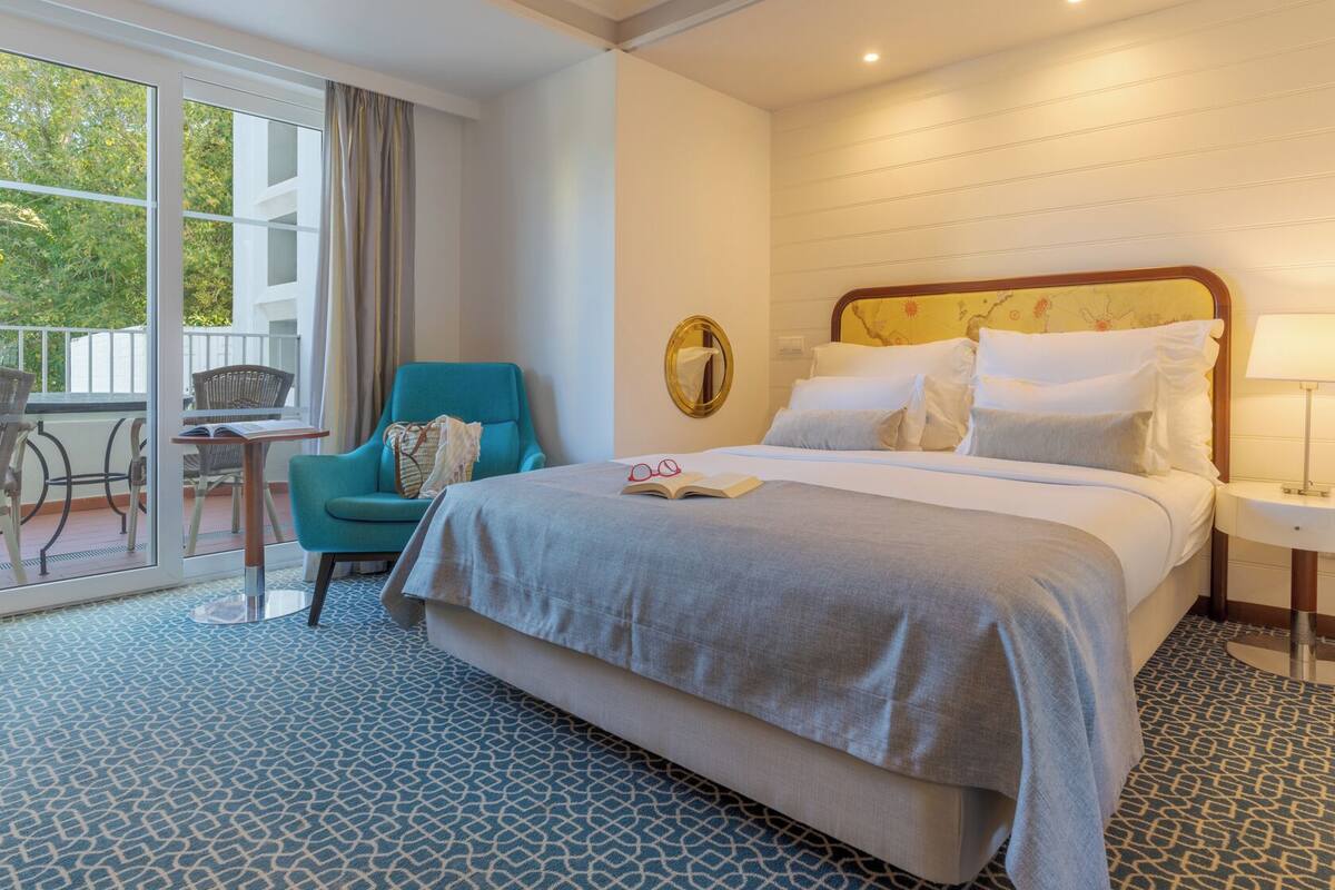 Ein Hotelzimmer mit Bett, Stuhl, Tisch und Blick durch eine Glastür.