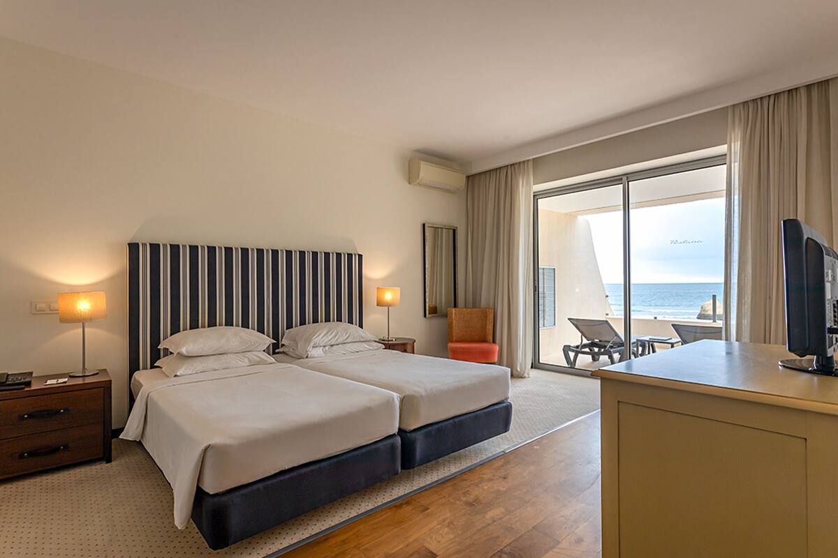 Ein Hotelzimmer mit zwei Betten, einem Schreibtisch, einem Stuhl und Meerblick.
