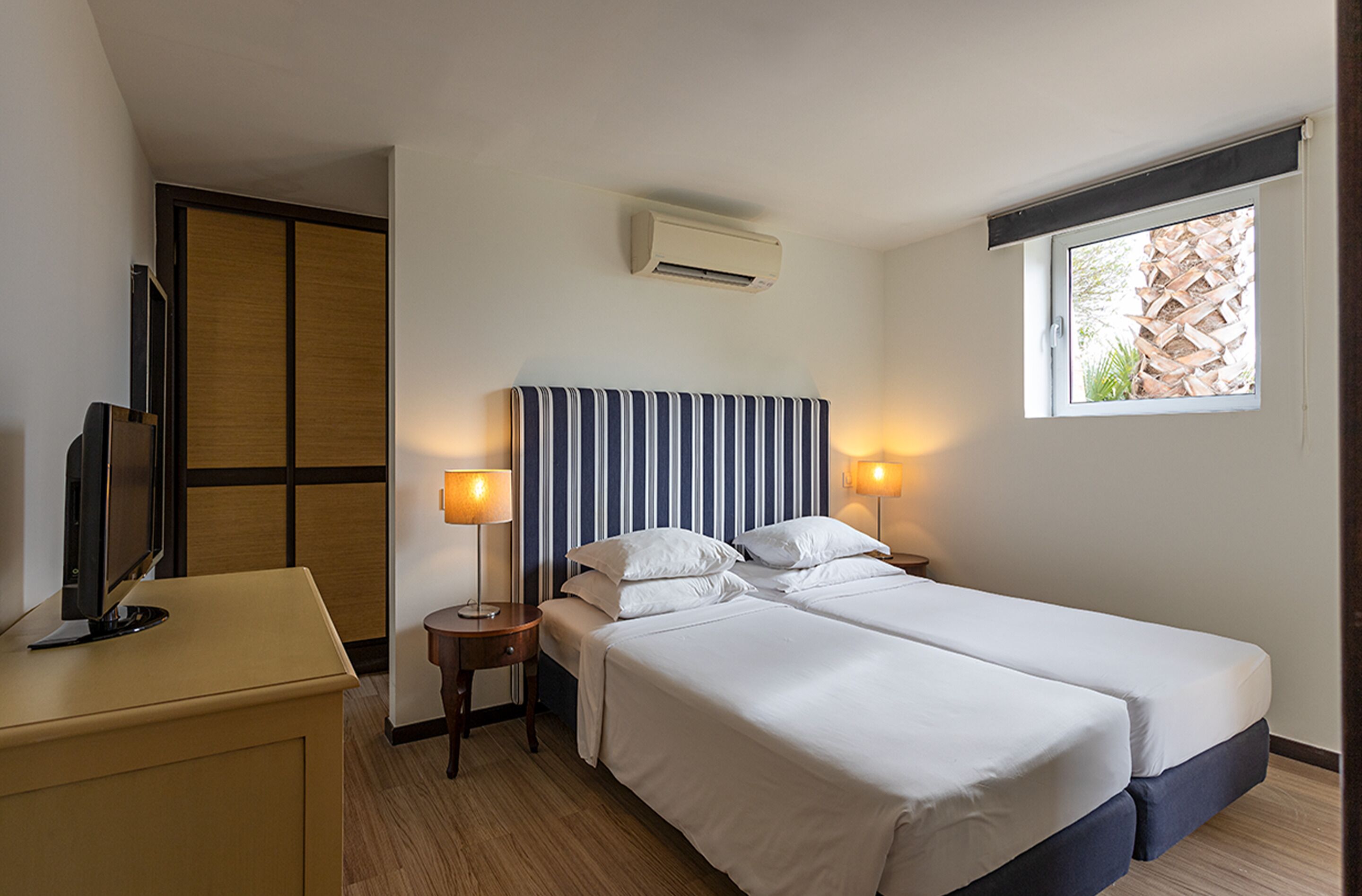 Hotelkamer met twee bedden, een televisie, een bureau en een raam met uitzicht op een houten constructie.
