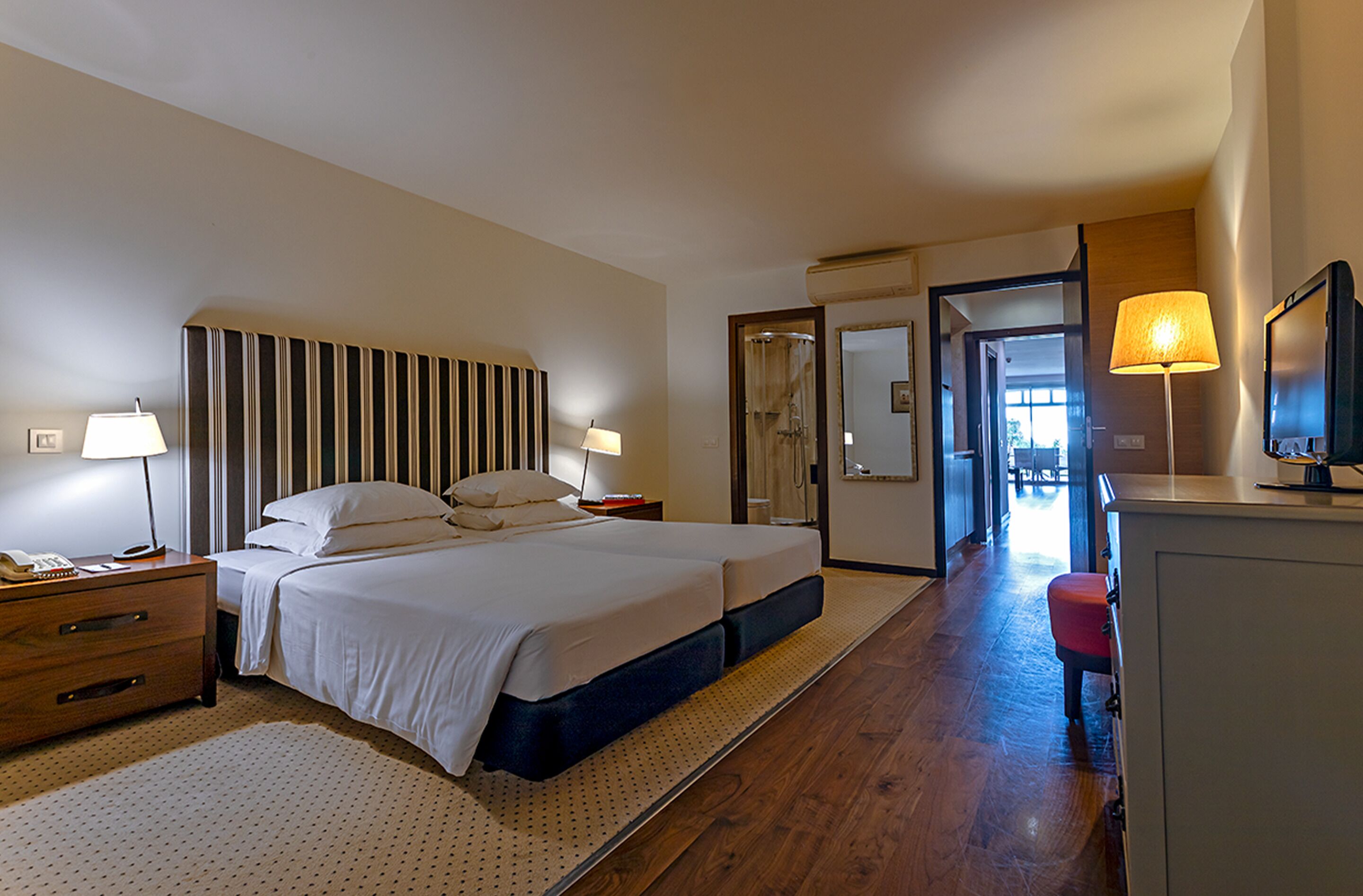 A hotel room with a large bed, bedside tables, a desk, and a mirror.