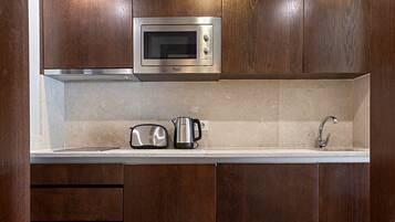 A kitchen with wooden cabinets, a stainless steel microwave, a toaster, a kettle, and a sink.