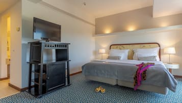 Una habitación de hotel con cama, lámparas de noche, un televisor sobre un soporte y un piso con diseño.