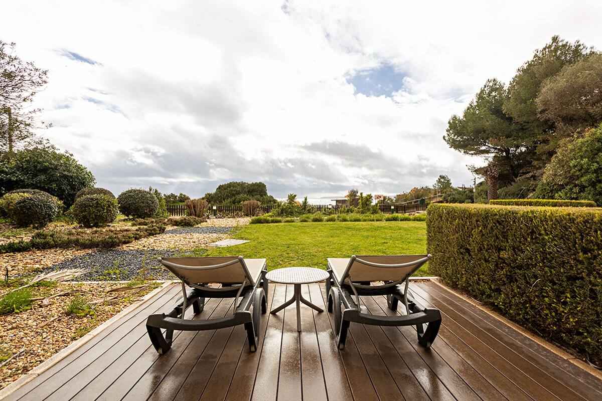 Eine Holzterrasse mit zwei Stühlen und einem Tisch mit Blick auf einen gepflegten Garten und eine Rasenfläche.