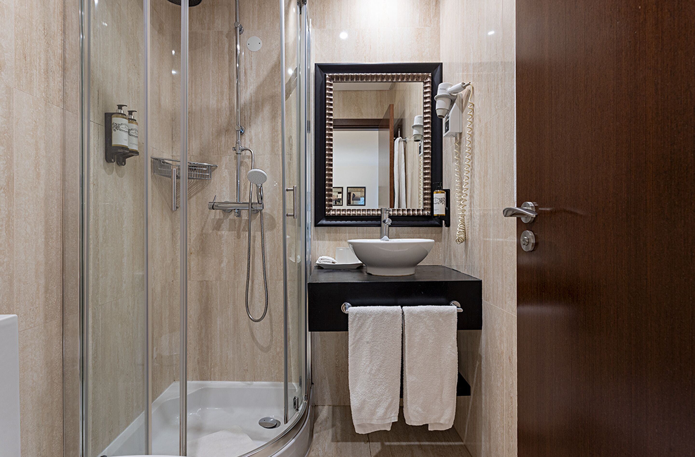 Une salle de bain moderne avec une douche à parois de verre, un lavabo avec un miroir au-dessus et une porte donnant sur une autre pièce.