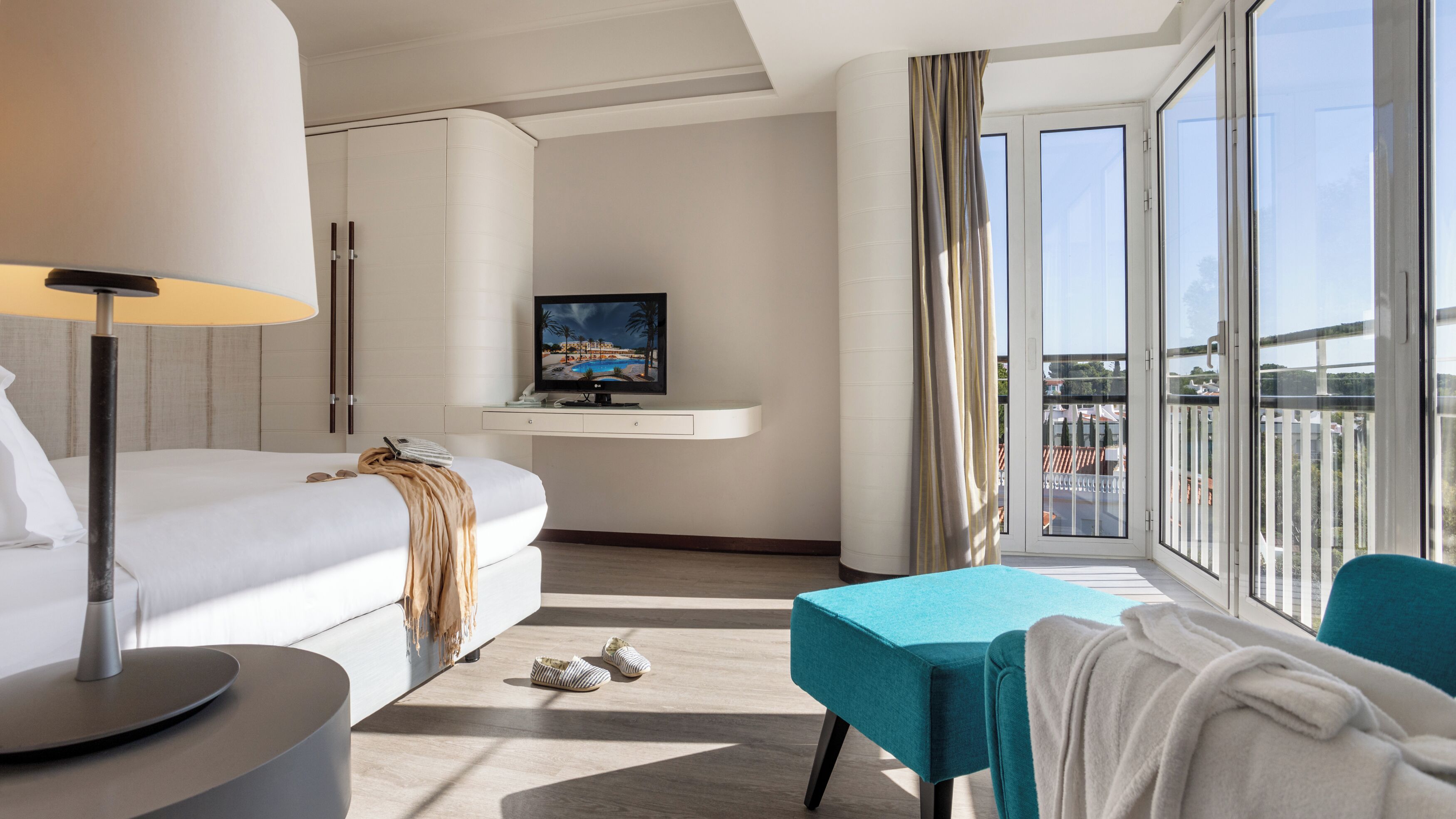 Et moderne hotelværelse med seng, skrivebord med computer, fjernsyn og balkon med udsigt.