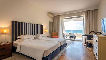 A hotel room with two beds, a desk, a chair, and a view of the ocean.