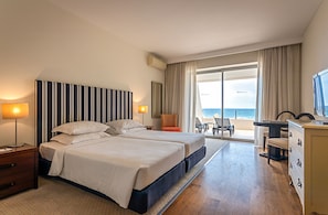 A hotel room with two beds, a desk, a chair, and a view of the ocean.