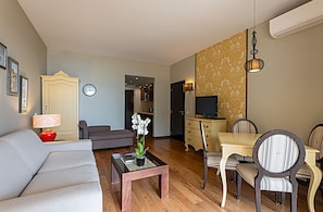 A modern living room with a sofa, coffee table, dining table with chairs, a TV, and a decorative plant.
