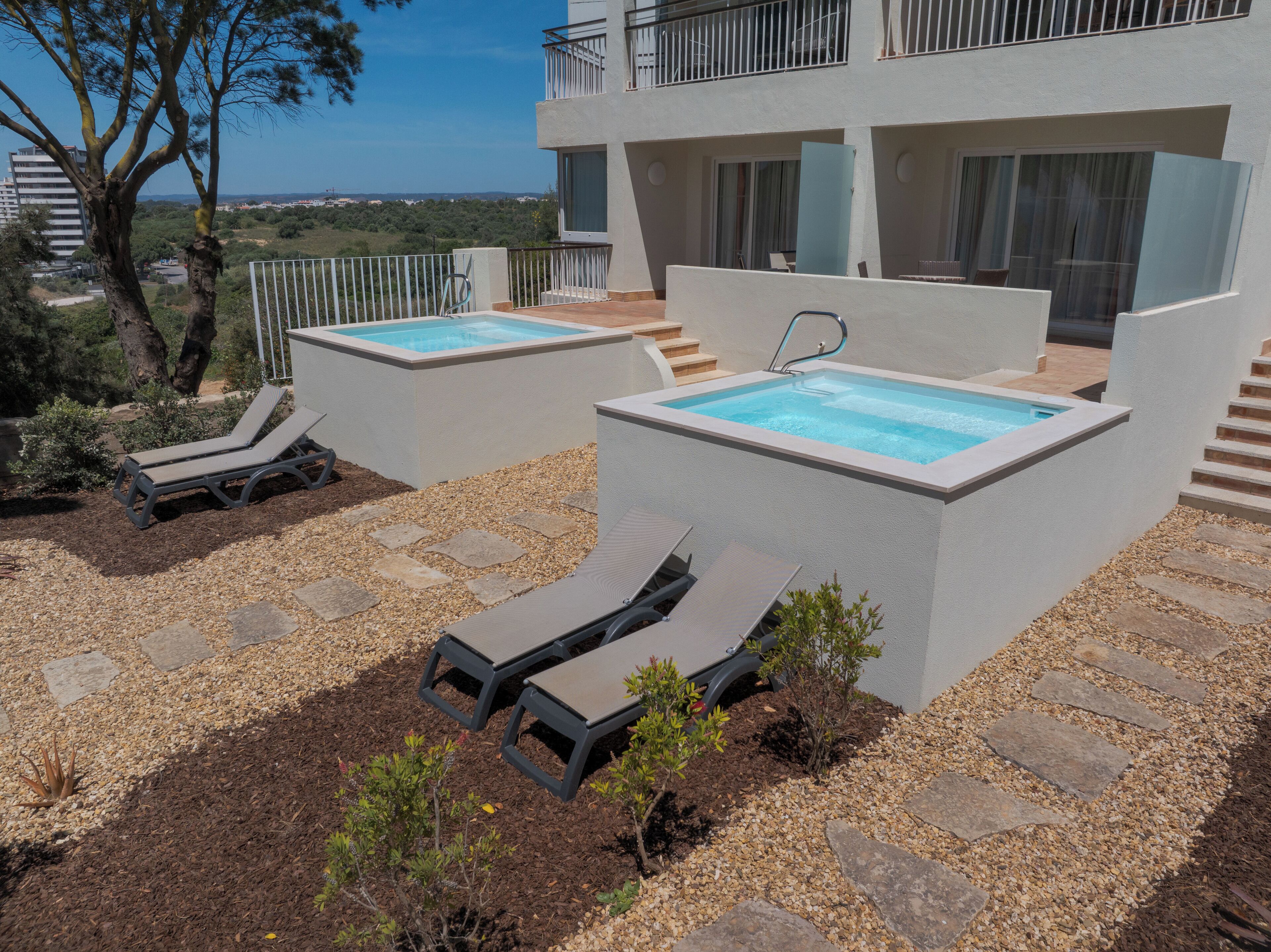 Zona de piscina exterior moderna amb dues piscines rectangulars, gandules i una escala que condueix a un balcó.