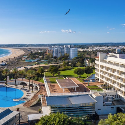 A coastal hotel with a swimming pool, a beach, and a view of the sea.