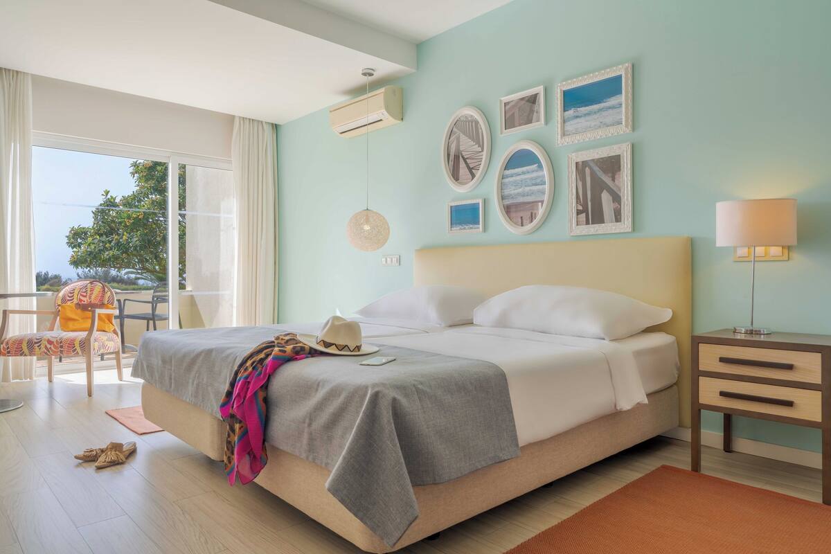 Ein Hotelzimmer mit Bett, Stuhl, Tisch und einem Balkon mit Aussicht.