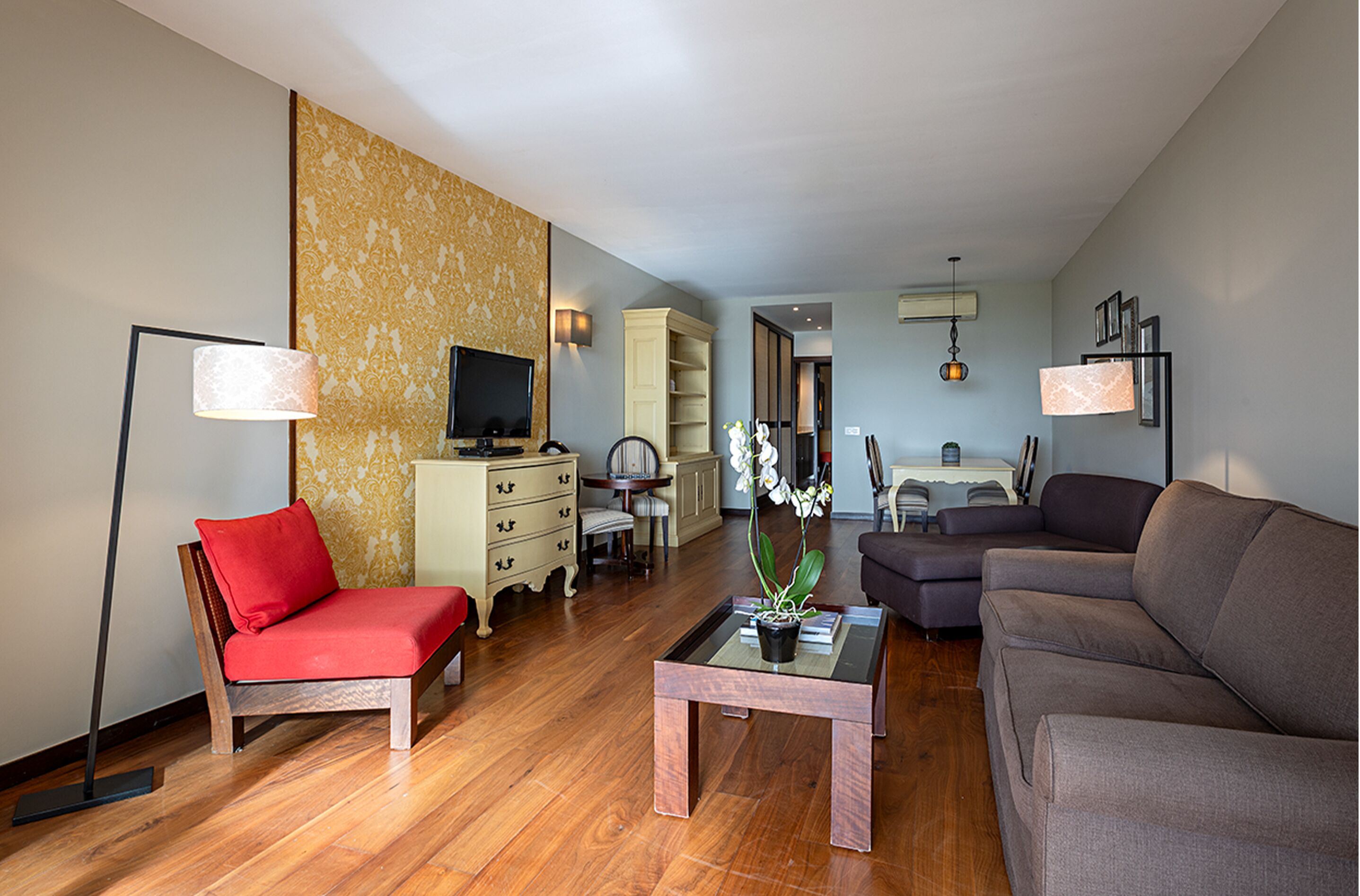 A modern living room with a red chair, a brown sofa, a glass coffee table, a television, and a bookshelf.