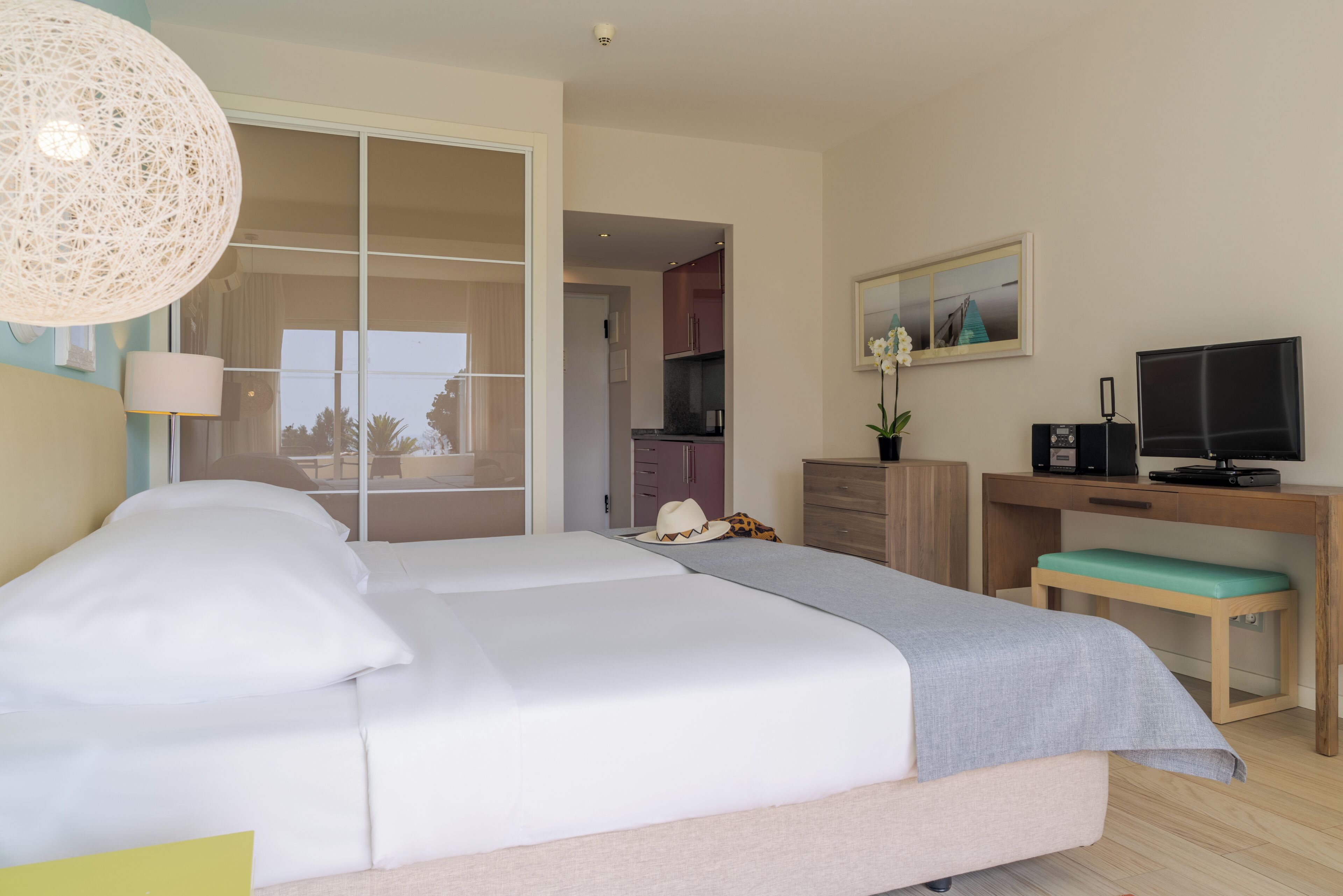 A bedroom with a bed, a desk, a television, and a view of the outside.