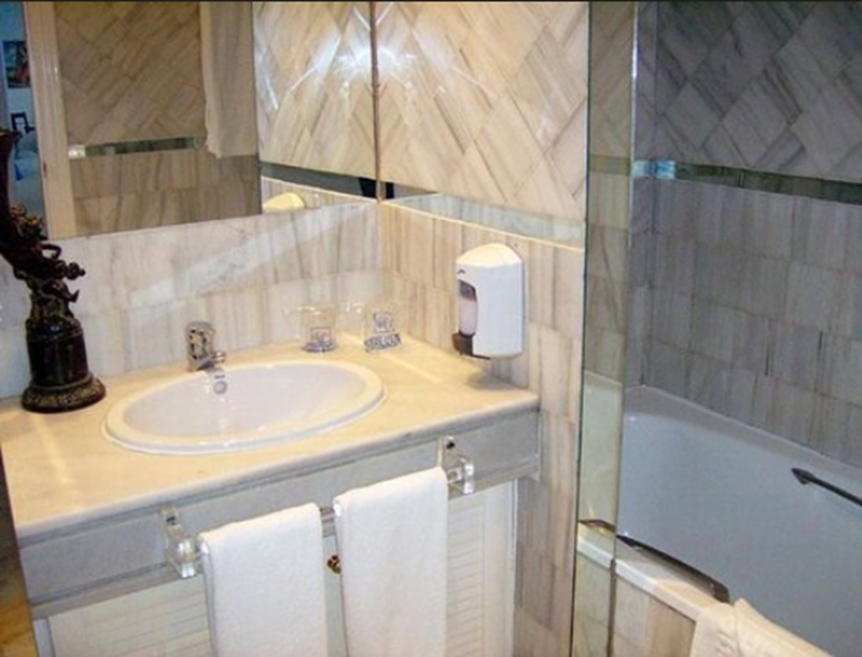Un bany amb un lavabo de marbre, un dosificador de sabó líquid i una cabina de dutxa de vidre.