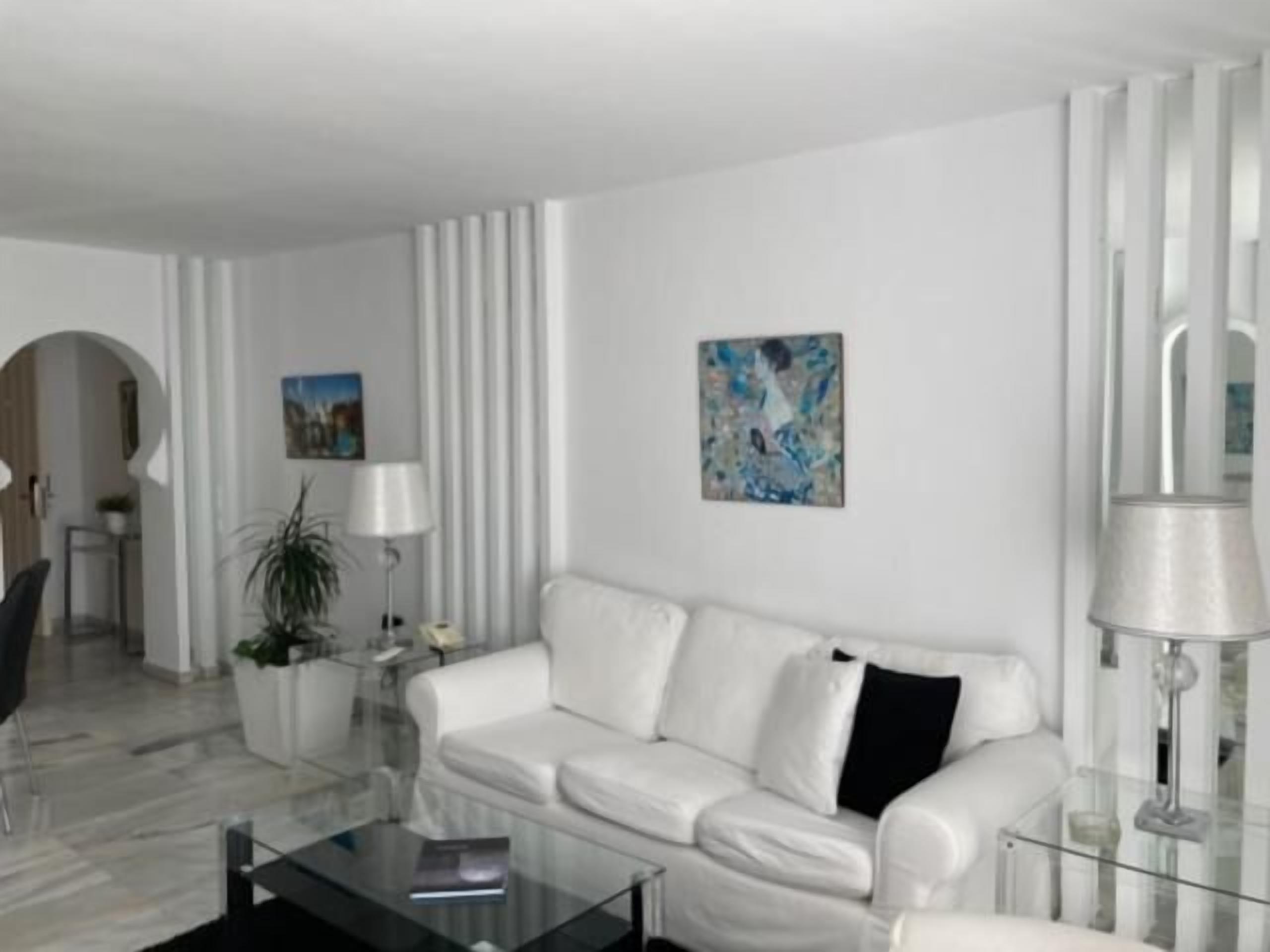 Een moderne woonkamer met een witte bank, een glazen salontafel en een schilderij aan de muur.